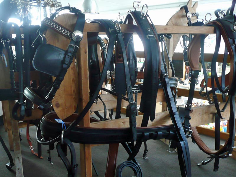 Schwarzes Pferdegeschirr mit Kopfstück auf Holzständer.